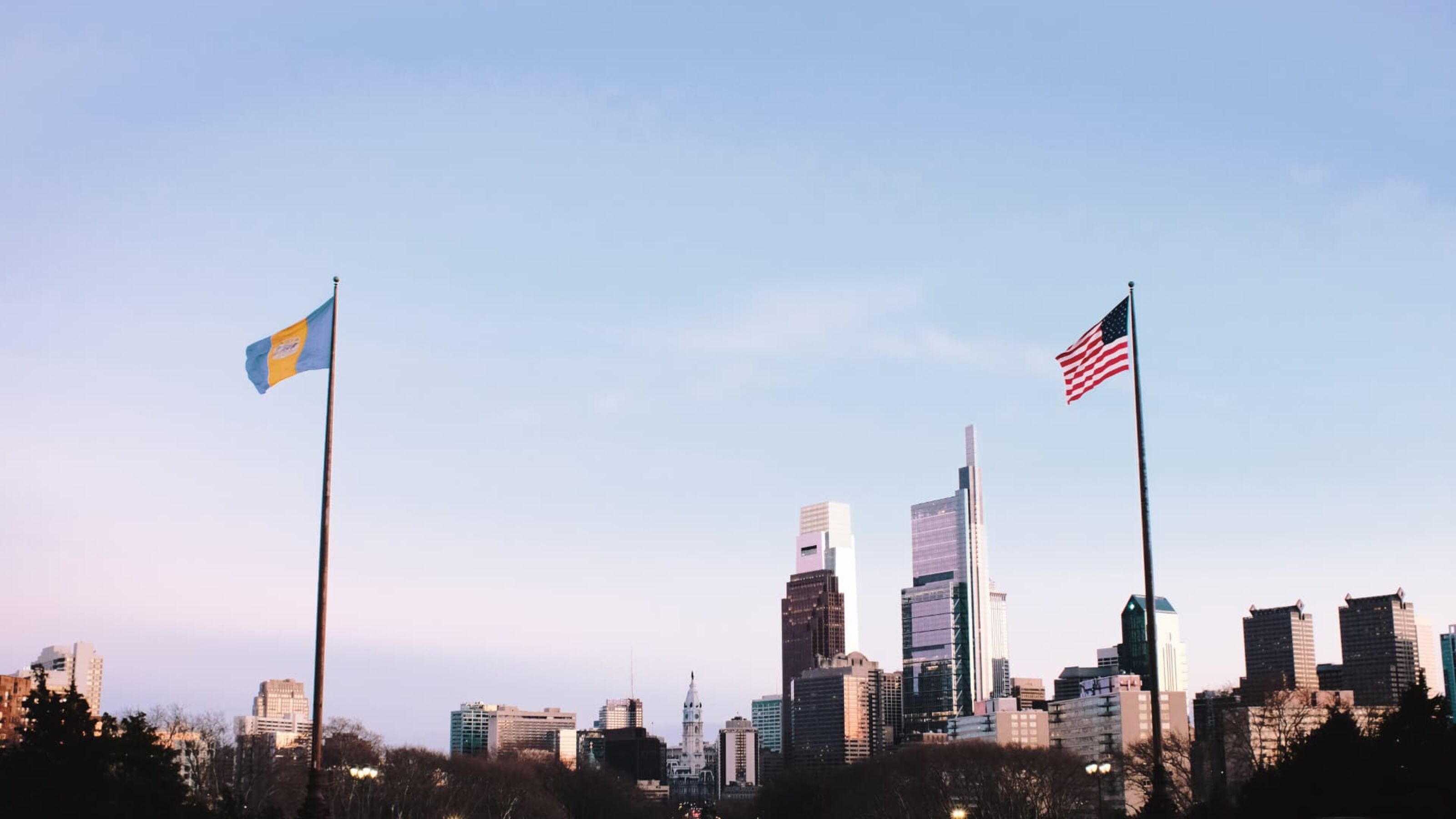 Philadelphia skyline at dusk with city and American flags in the foreground